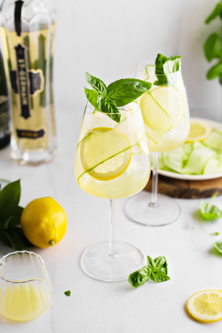 two glasses of st. germain spritz next to fresh lemons and basil sprigs