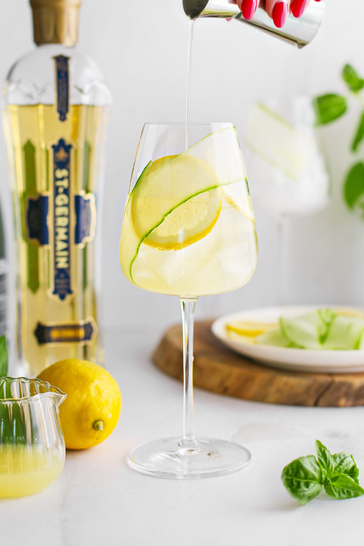 woman adding st germain to a glass with prosecco and lemon juice to prepare a recipe for St. Germain prosecco spritz
