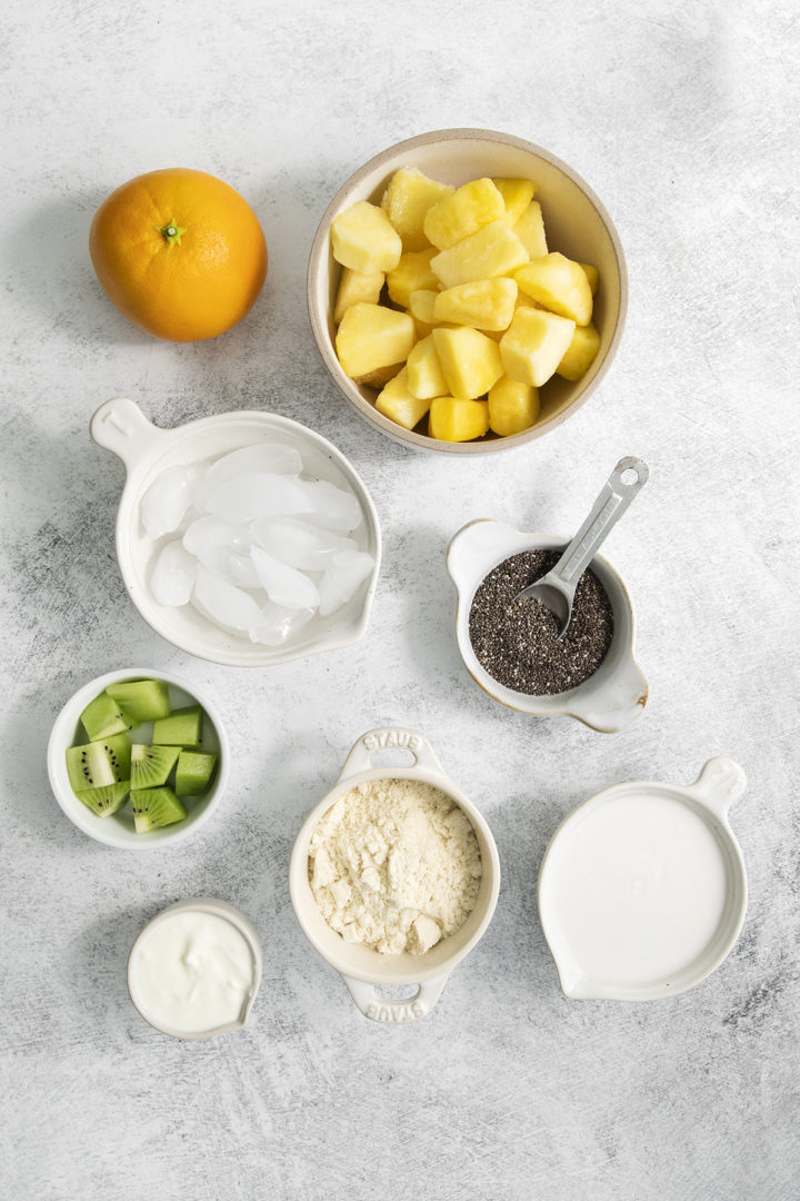 overhead photo of ingredients for this pineapple orange smoothie recipe arranged in white bowls on a light background