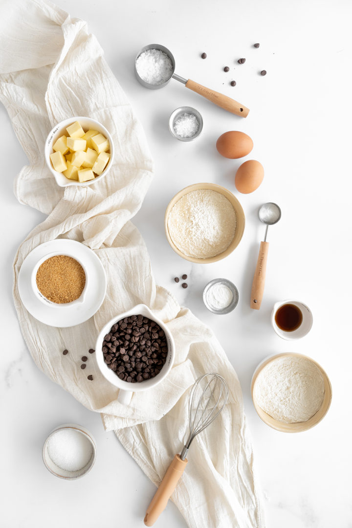 ingredients needed to make the ny times chocolate chip cookies arranged in bowls on a marble counter