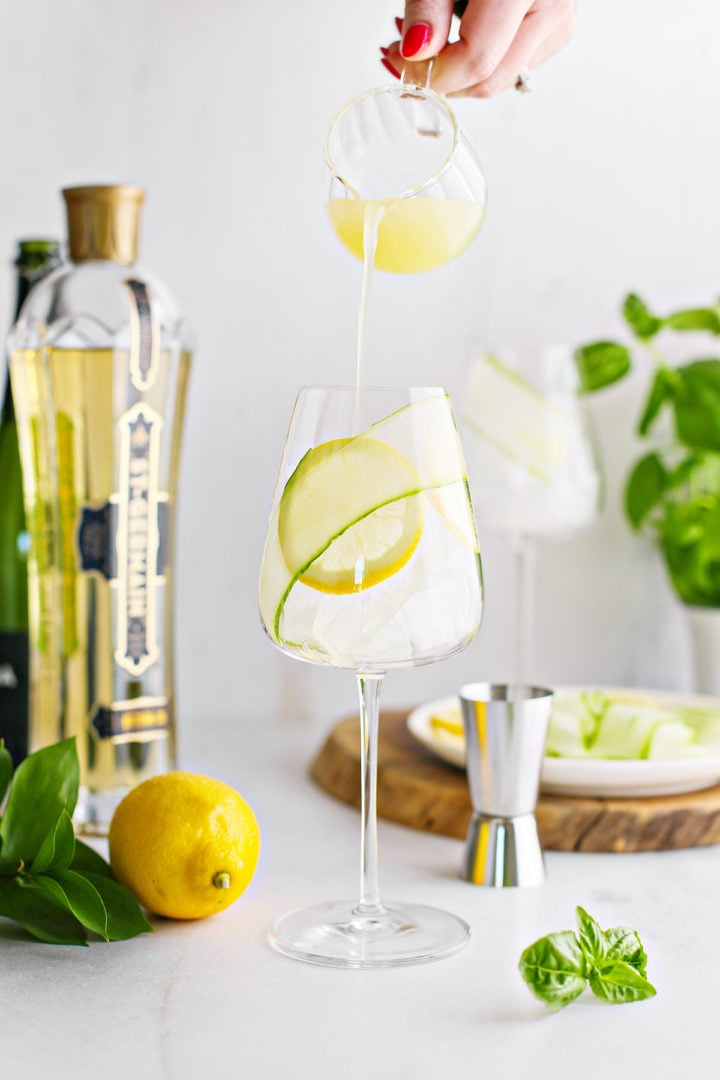 woman adding fresh lemon juice to a wine glass to make a elderflower prosecco cocktail