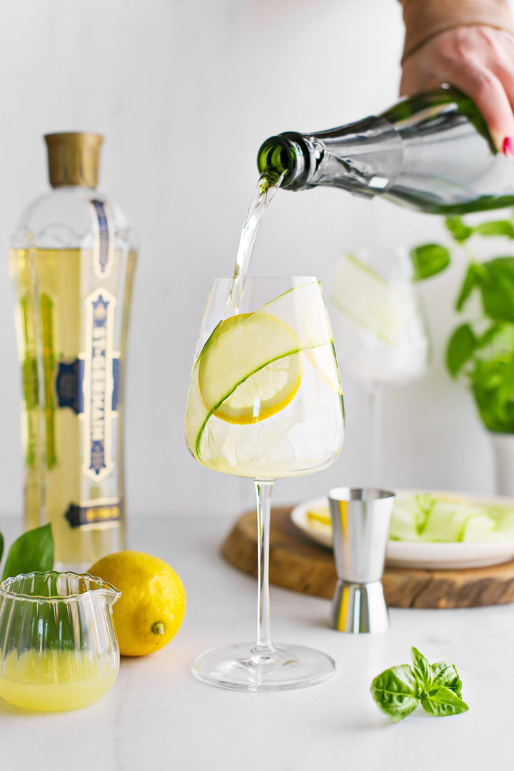 woman adding prosecco to a glass of lemon juice to make a st germain spritz