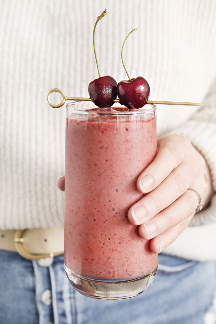 woman holding a glass of a mango cherry smoothie