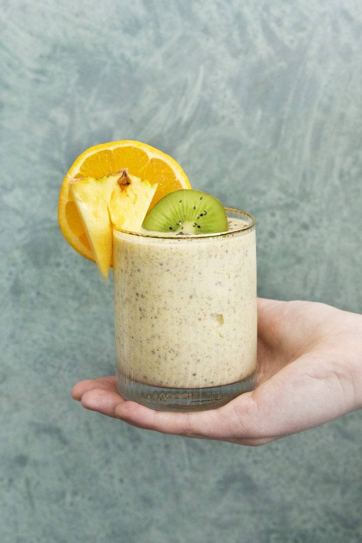 woman holding a glass of a pineapple orange smoothie against a teal background