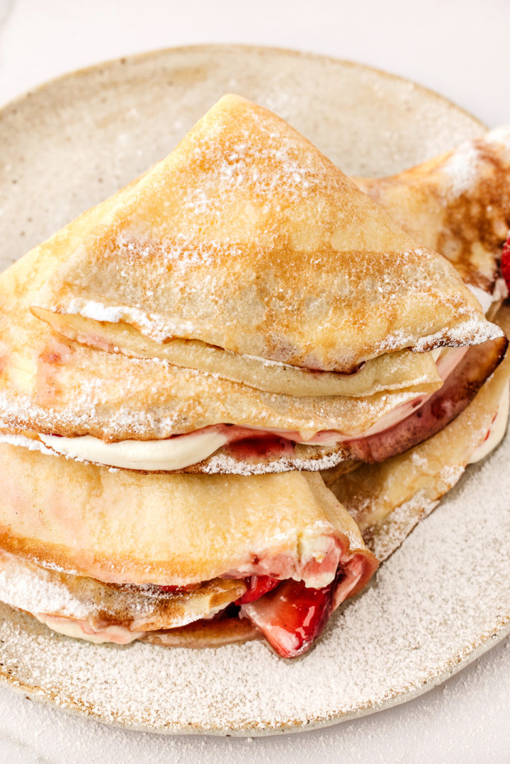 strawberry filled crepes on a plate with powdered sugar