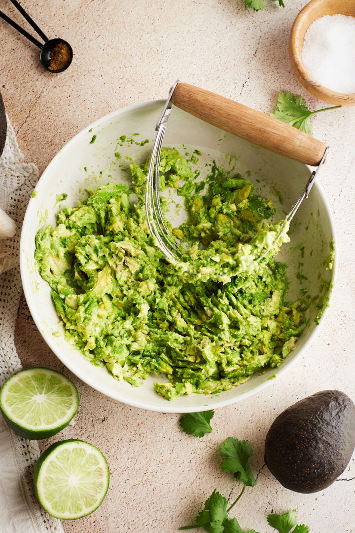 mashed ripe avocado in a white bowl for a simple guac recipe 
