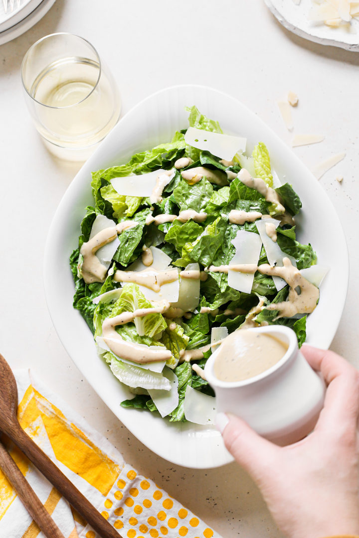 traditional Caesar salad dressing being poured onto salad