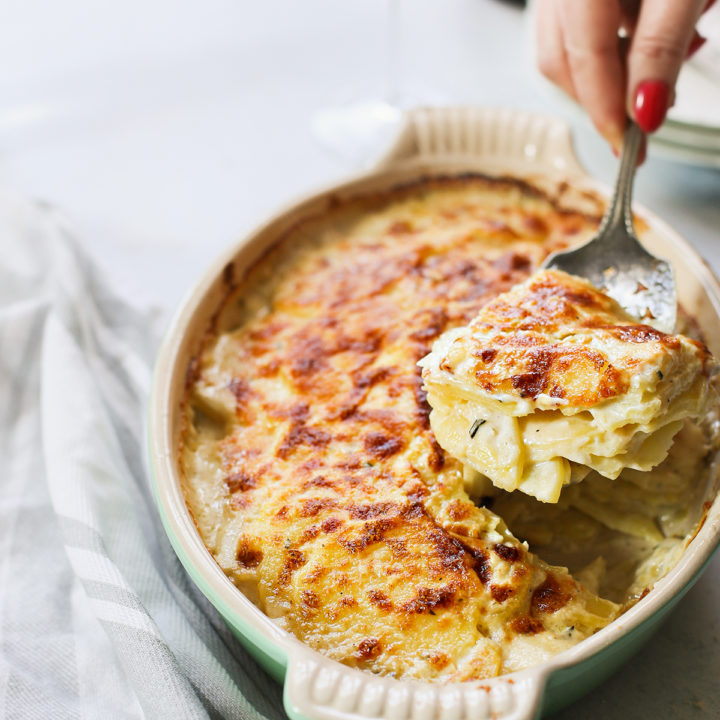 woman serving scalloped potatoes from a baking dish