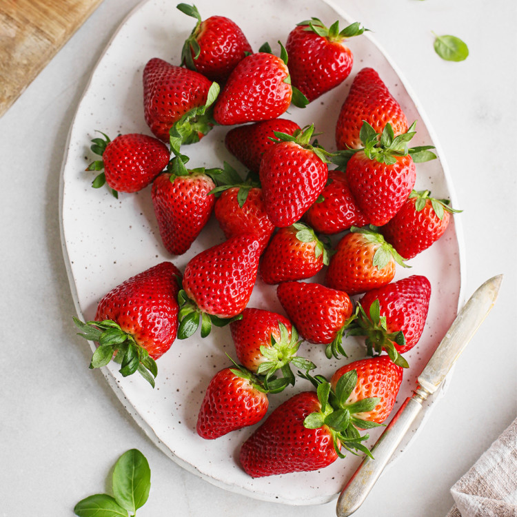 photo of spring strawberries on a white platter with a knife