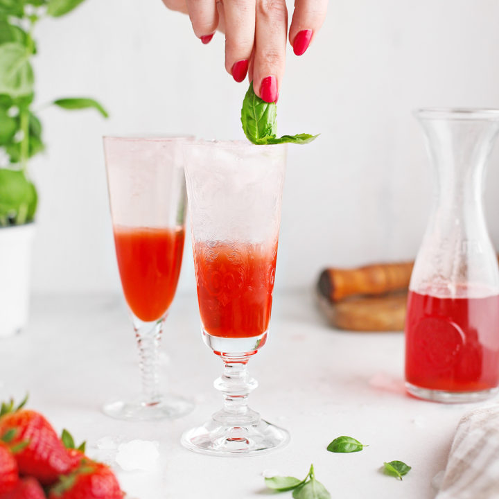 woman garnishing a strawberry shrub cocktail with fresh basi leaves