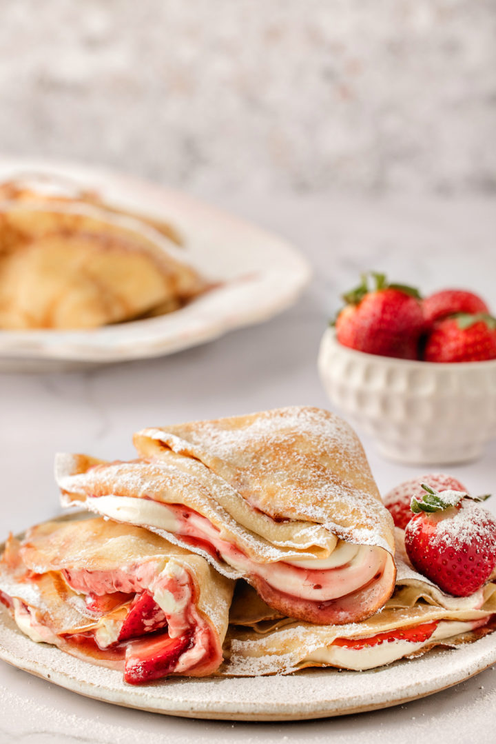 a plate of strawberry crepes with a bowl of fresh strawberries