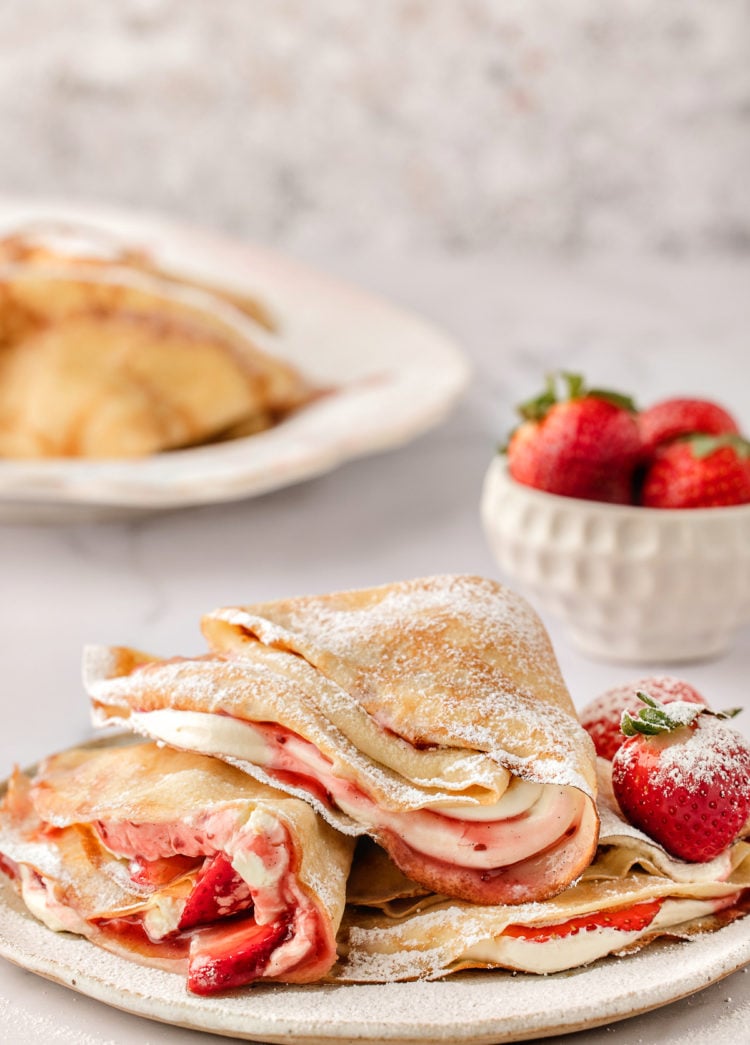 a plate of strawberry crepes with a bowl of fresh strawberries