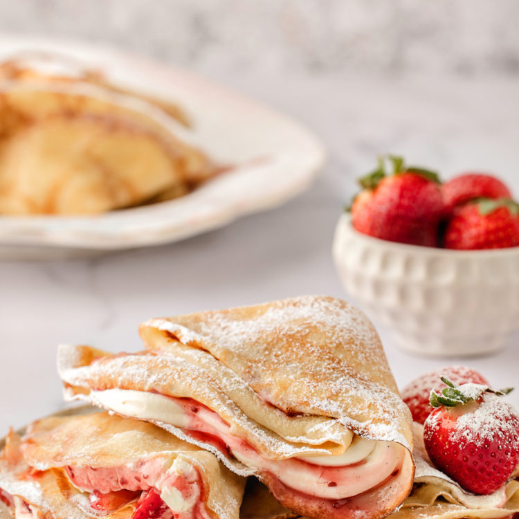 a plate of strawberry crepes with a bowl of fresh strawberries