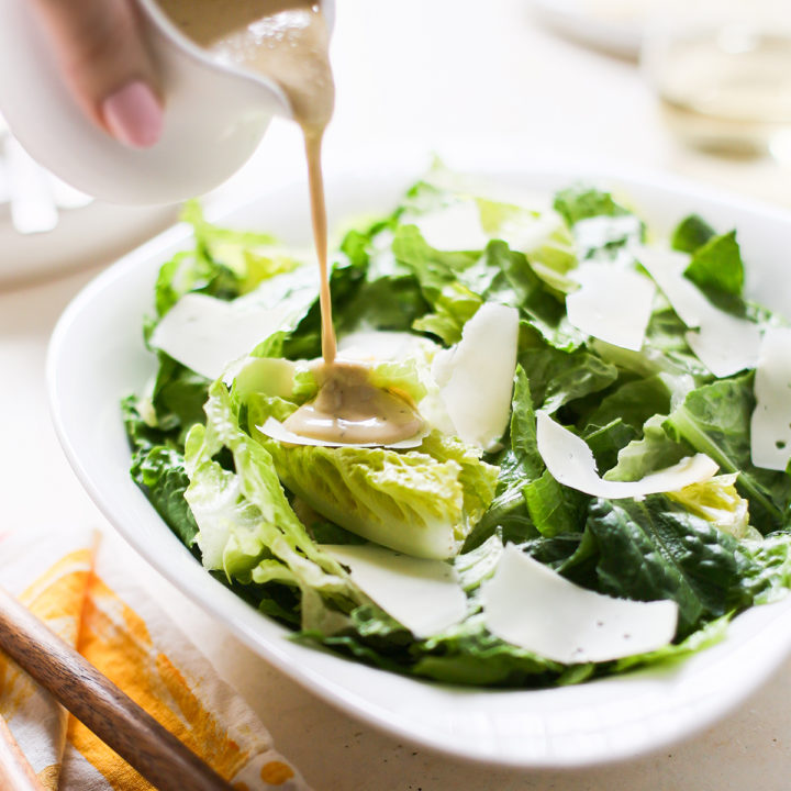 woman pouring dressing onto homemade caesar salad