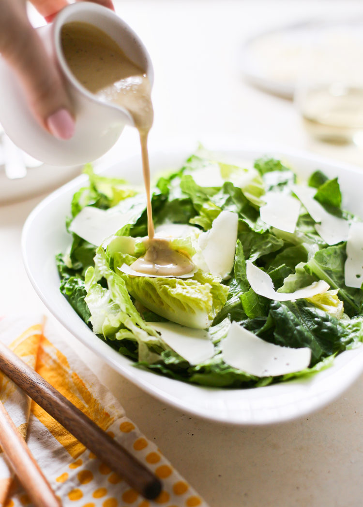 woman pouring dressing onto homemade caesar salad