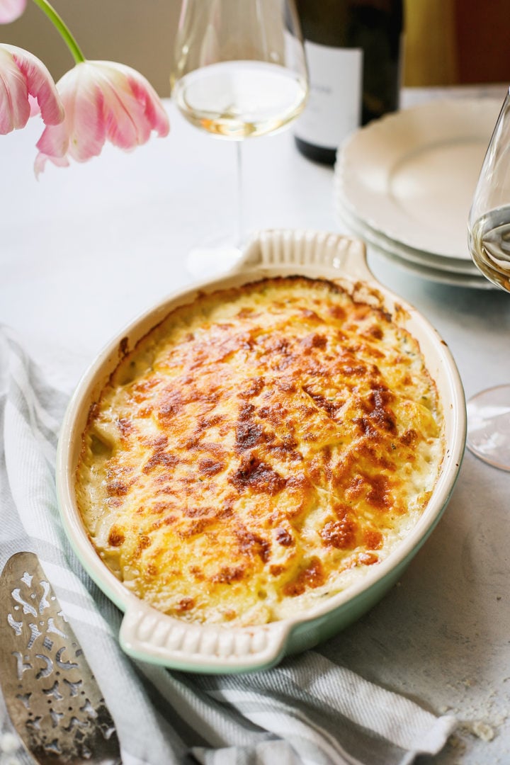 a table set with a casserole dish of parmesan scalloped potatoes, plates, and glass of wine