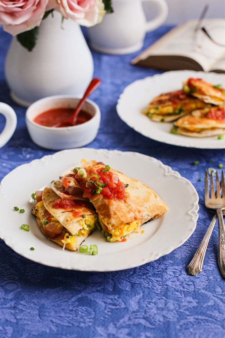 breakfast table set with scrambled egg quesadillas on two white plates and a bowl of salsa 