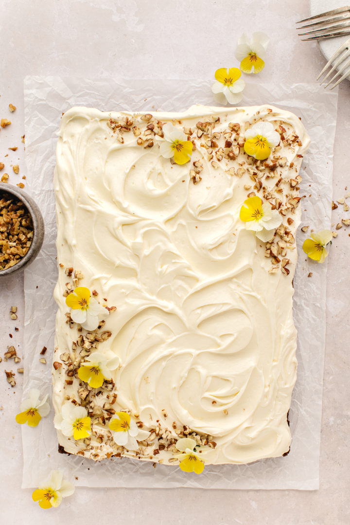 overhead photo of a pineapple carrot cake with cream cheese frosting that is decorated with nuts