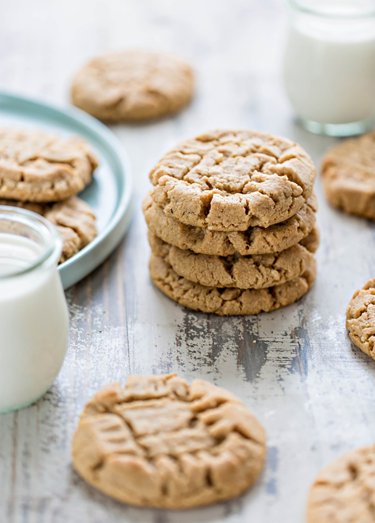 a stack of almond butter cookies on a wooden table with glasses of milk