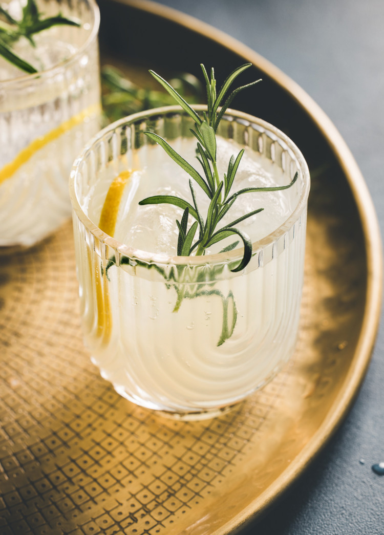 two glasses of a gin sour cocktail on a gold tray garnished with rosemary and lemon