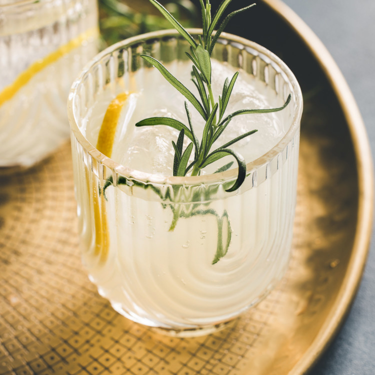 two glasses of a gin sour cocktail on a gold tray garnished with rosemary and lemon