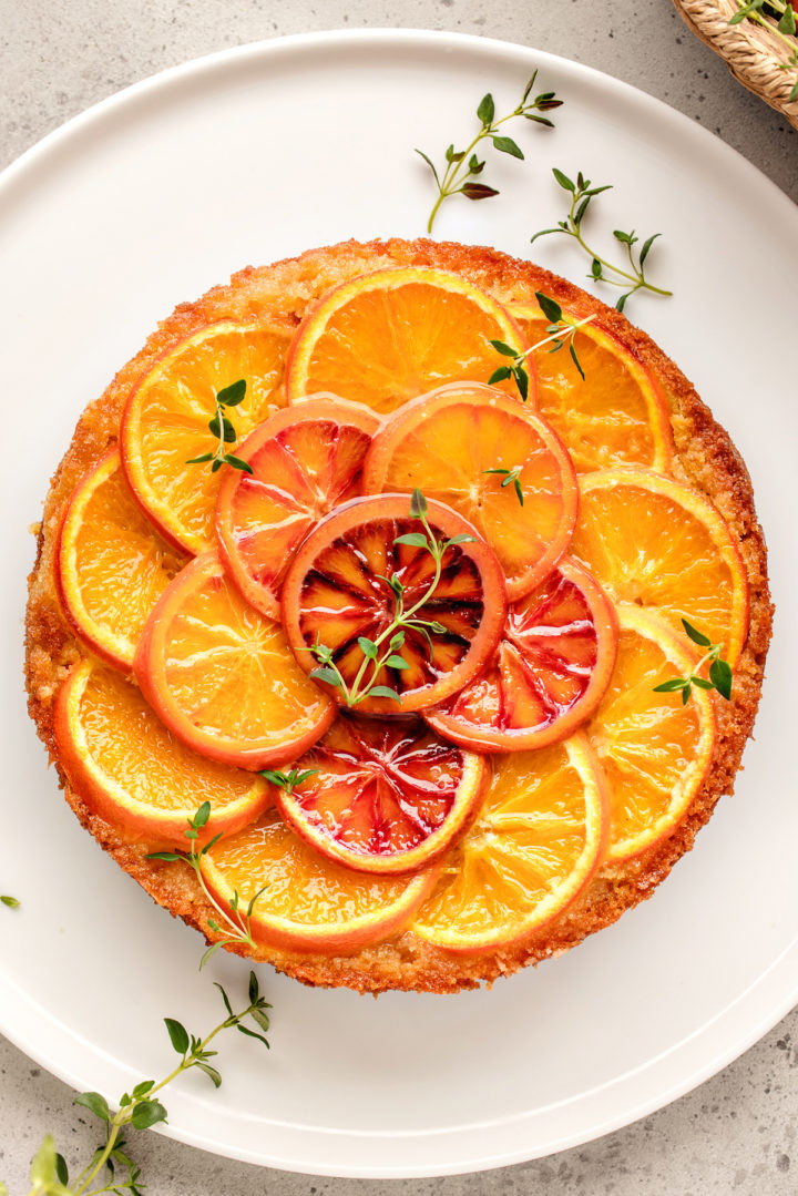 orange upside down cake on a white serving plate decorated with fresh thyme