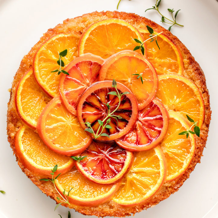 orange upside down cake on a white plate decorated with fresh thyme