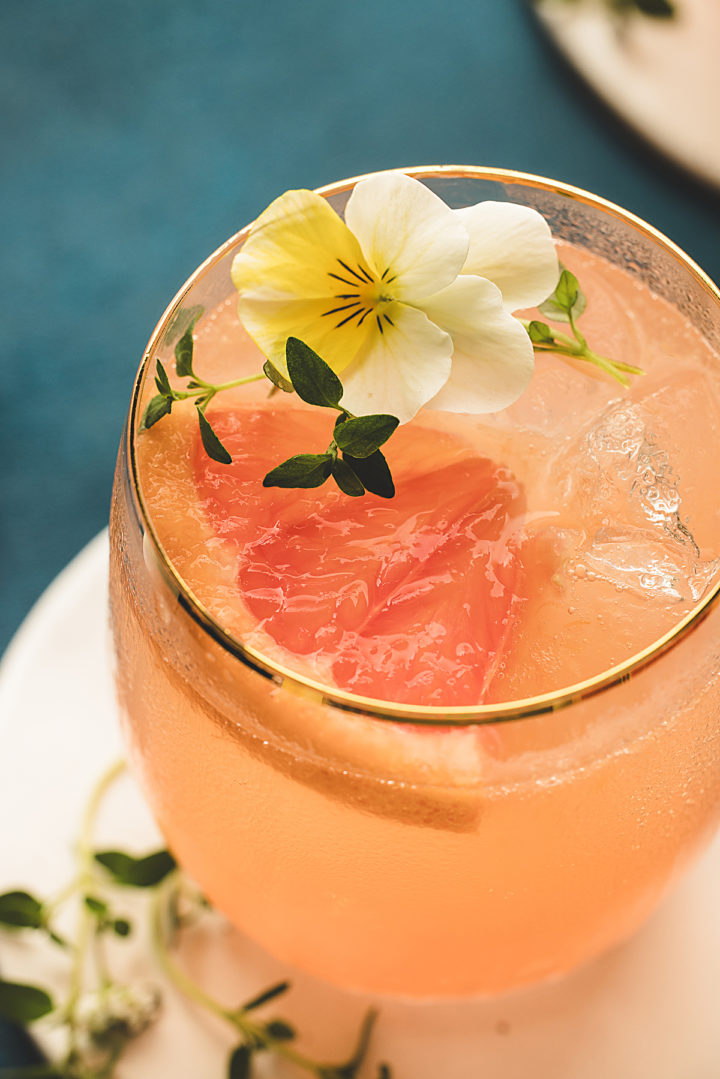 close up photo of a grapefruit gin and tonic in a glass garnished with edible flowers and fresh thyme