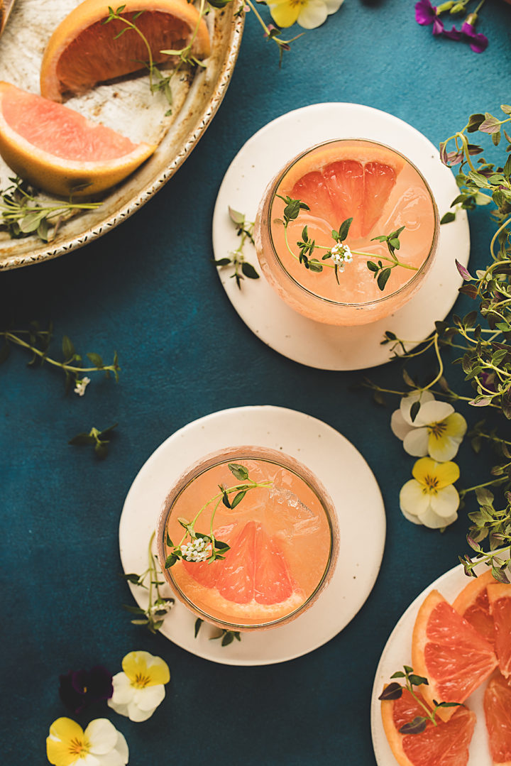 overhead photo of glasses of grapefruit gin and tonic surrounded by fresh thyme sprigs and grapefruit slices