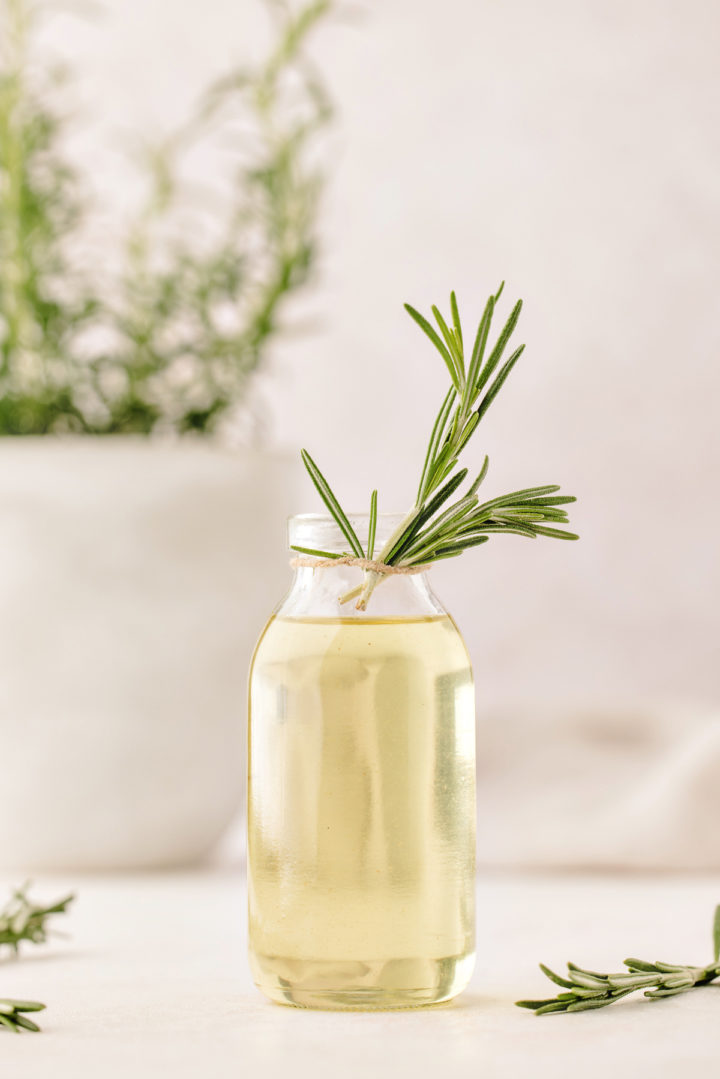 rosemary cocktail syrup in a glass bottle with rosemary plant in the background