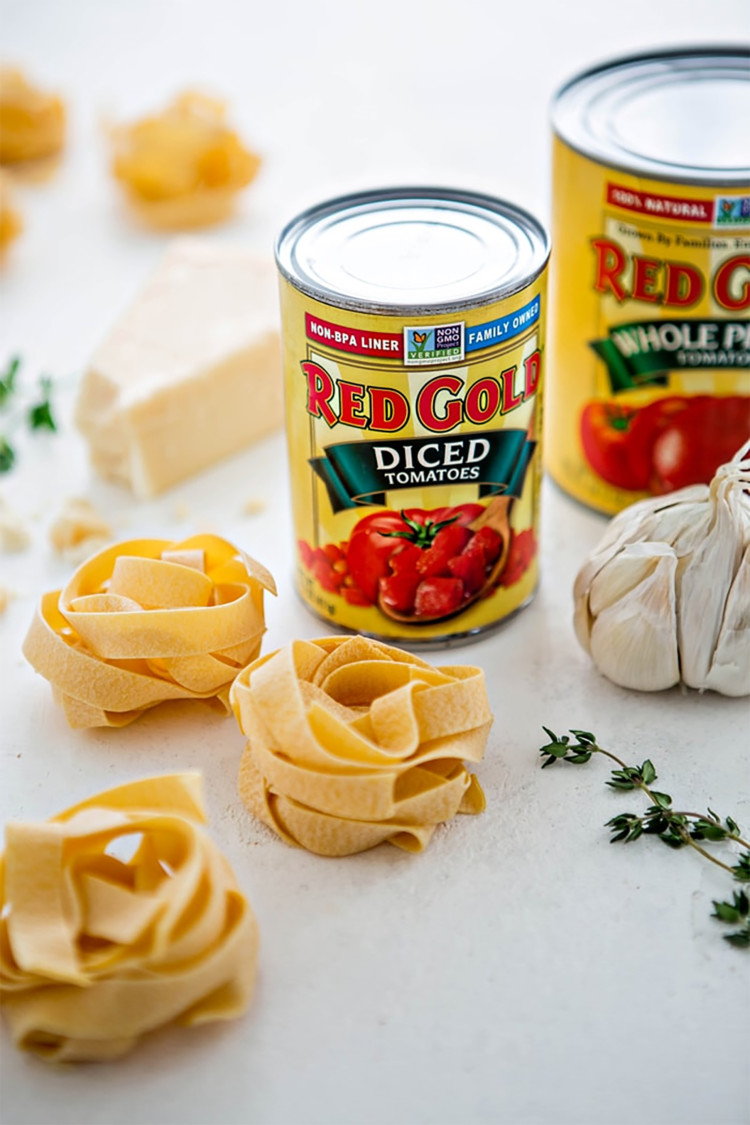 two cans of red gold tomatoes next to pasta, fresh herbs, and garlic