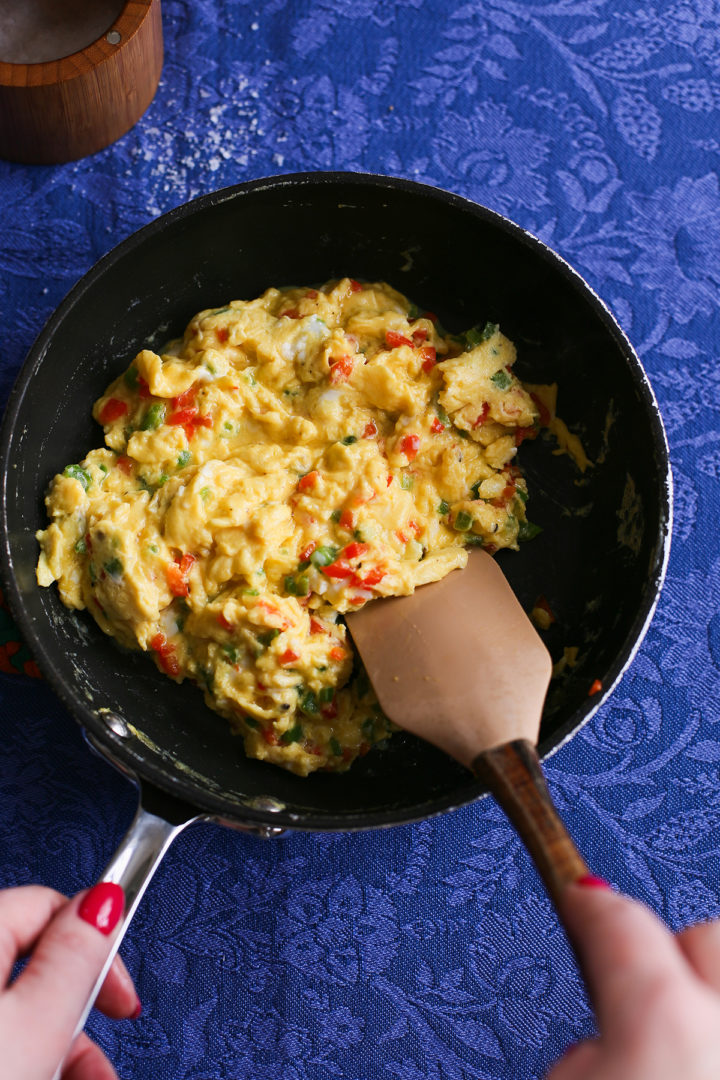 woman stirring peppers into a pan with scrambled eggs to make scrambled egg quesadillas
