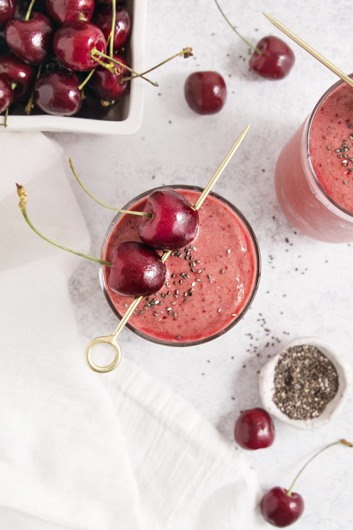overhead photo of a mango cherry smoothie garnished with fresh cherries and chia seed