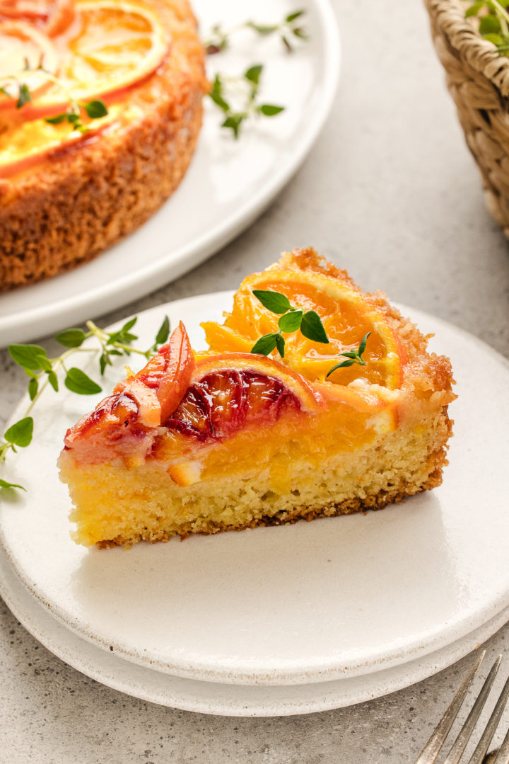slice of orange upside down cake on a white plate with a fresh thyme sprig garnish