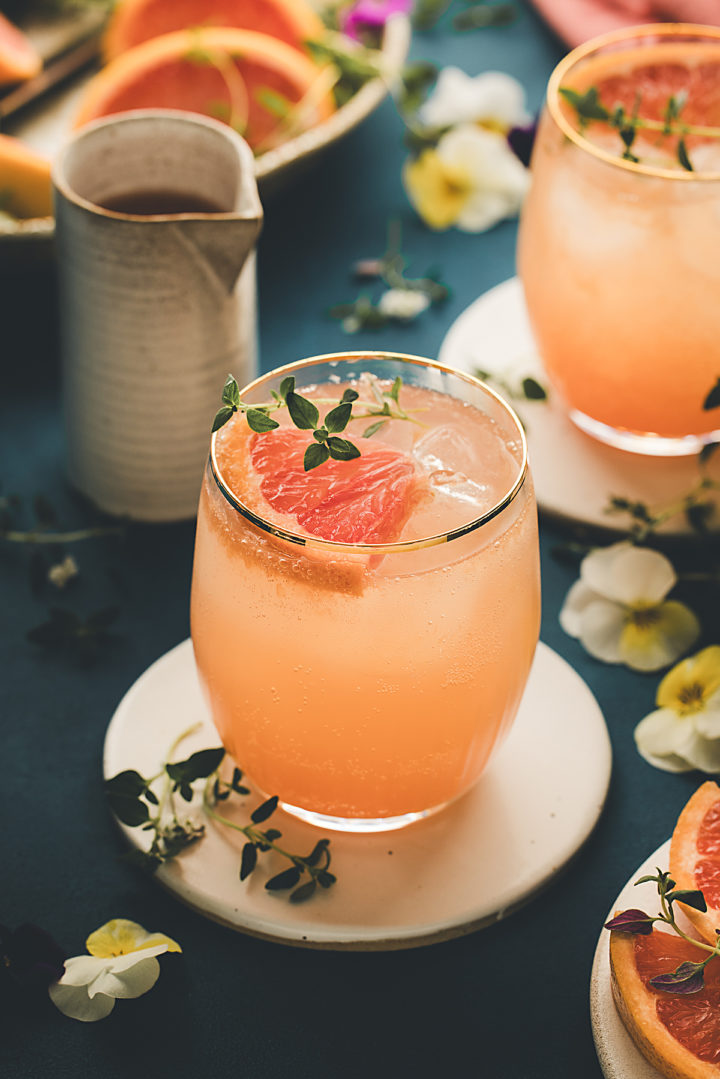 table set with glasses of grapefruit gin and tonic garnished with fresh grapefruit slices, thyme sprigs, and edible flowers