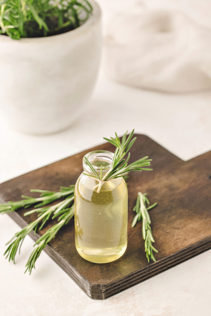 a glass jar of rosemary simple syrup on a wooden cutting board surrounded by fresh rosemary sprigs