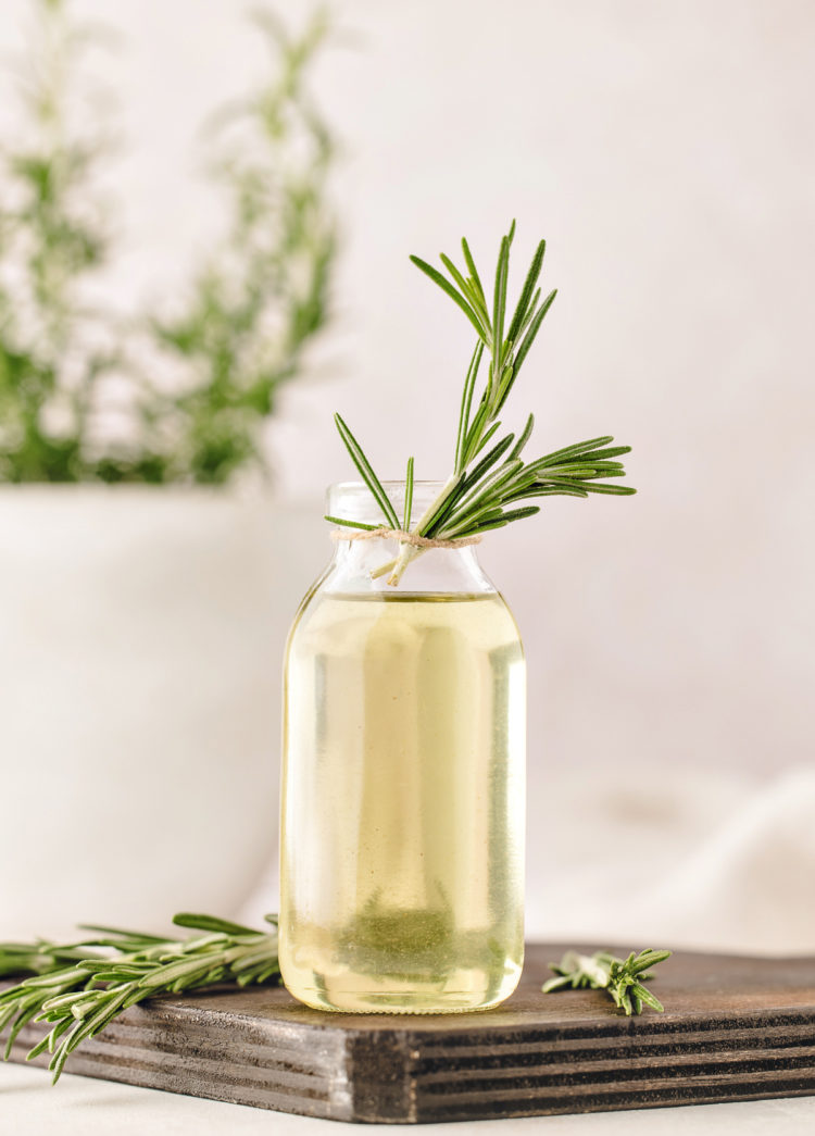 rosemary simple syrup in a clear glass jar on a wooden cutting board garnished with fresh rosemary sprigs