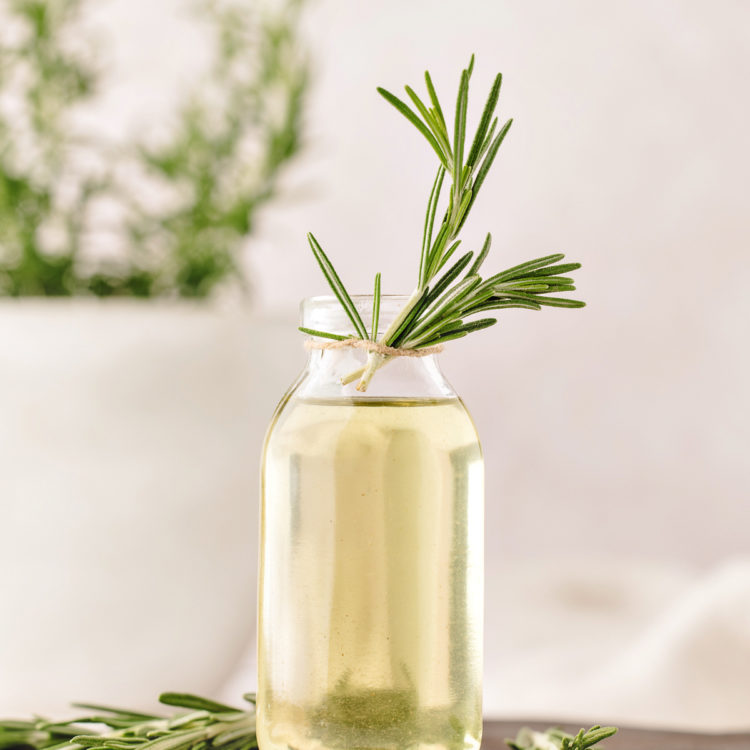 rosemary simple syrup in a clear glass jar on a wooden cutting board garnished with fresh rosemary sprigs
