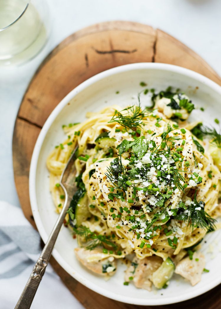 chicken pasta primavera in a white bowl on a wooden board