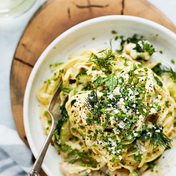 chicken pasta primavera in a white bowl on a wooden board