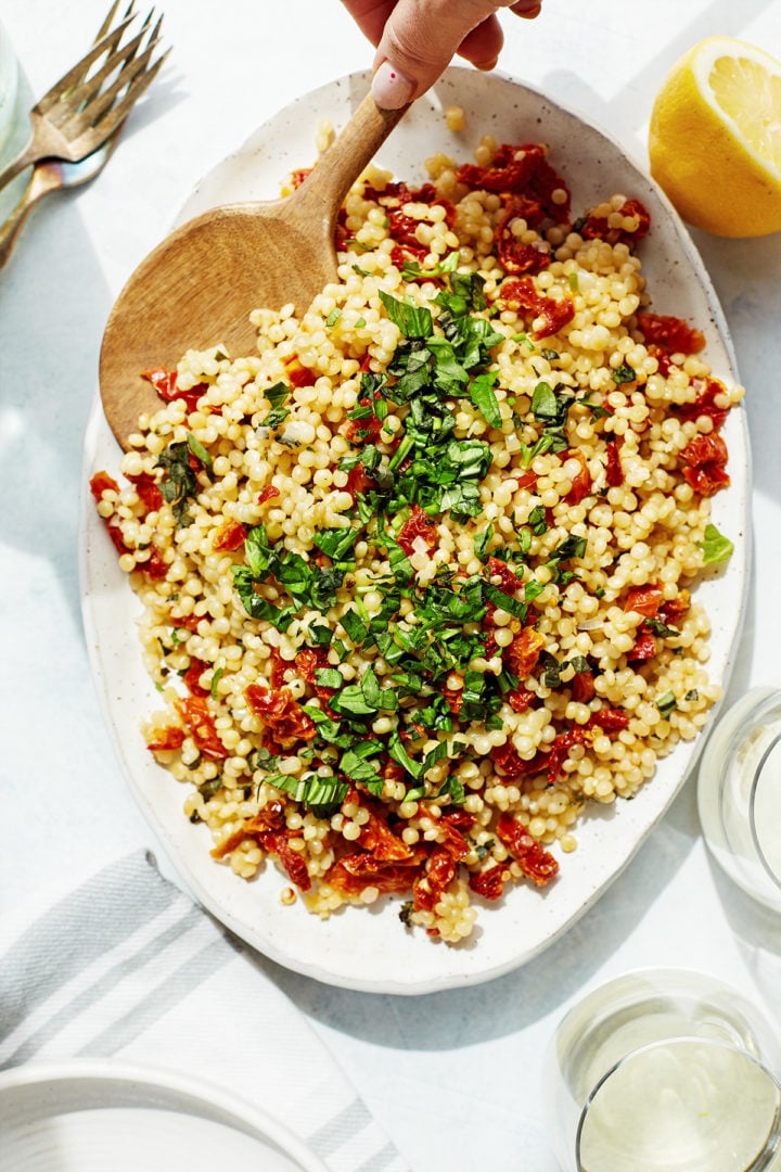 woman serving pearl couscous salad with a wooden spoon