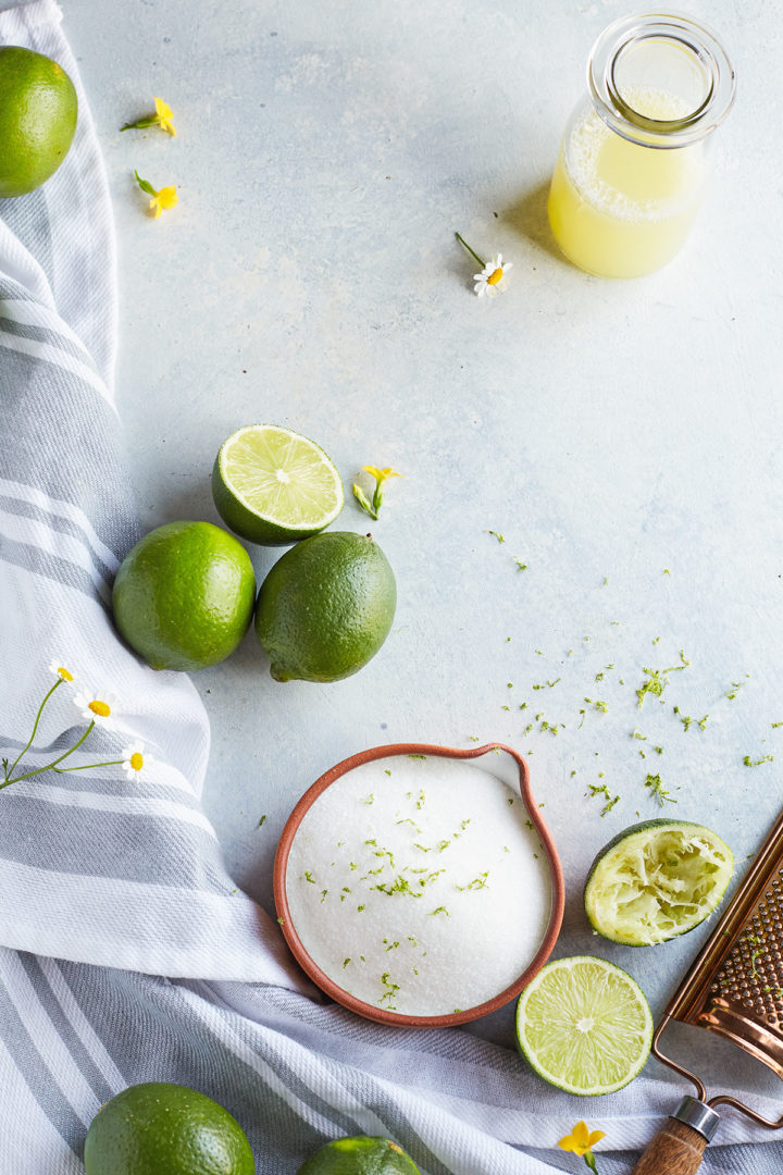 bowl of sugar, fresh limes, and lime juice arranged on a background