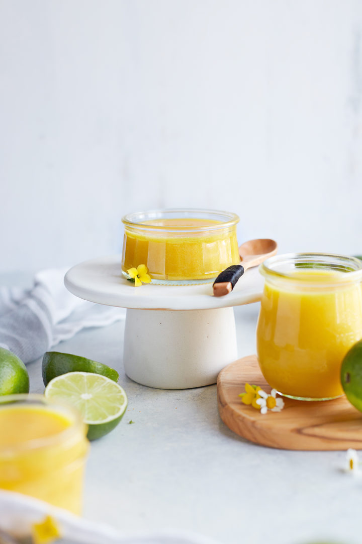 3 jars of lime curd arranged on a wooden board and a small white platter