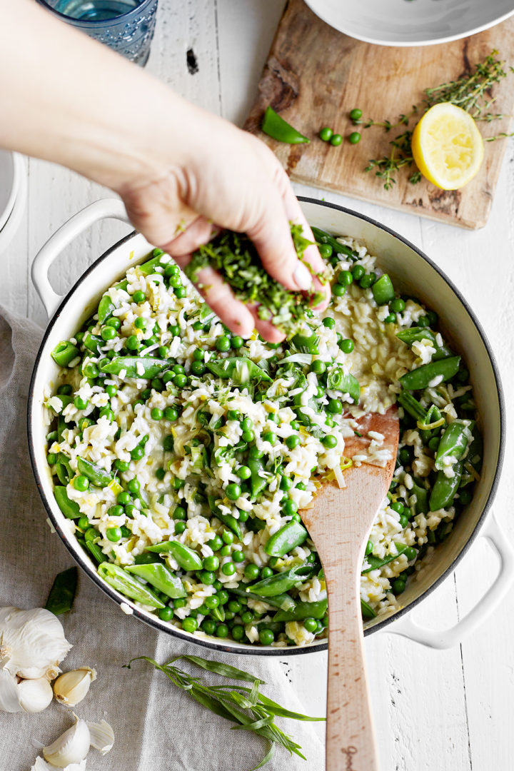 woman adding fresh herbs to a pan of spring pea risotto