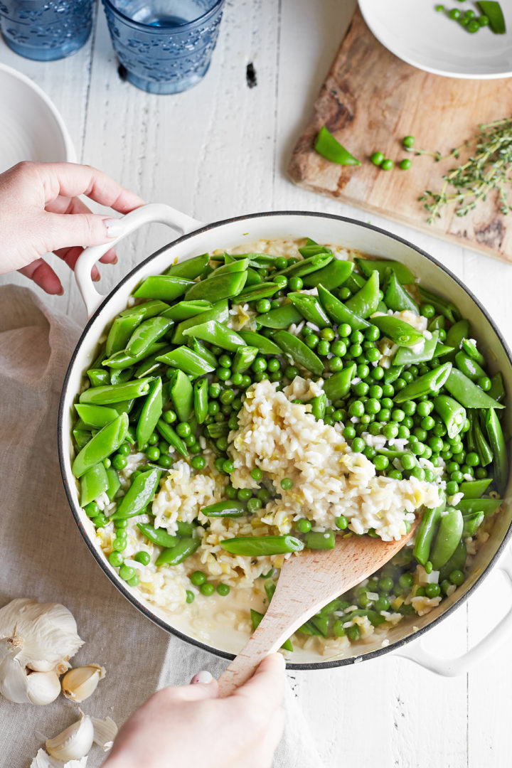 woman stirring spring peas into risotto