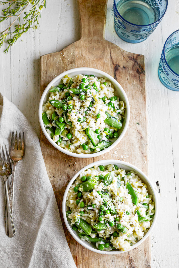 overhead photo of pea risotto in two white bowls on a wooden board