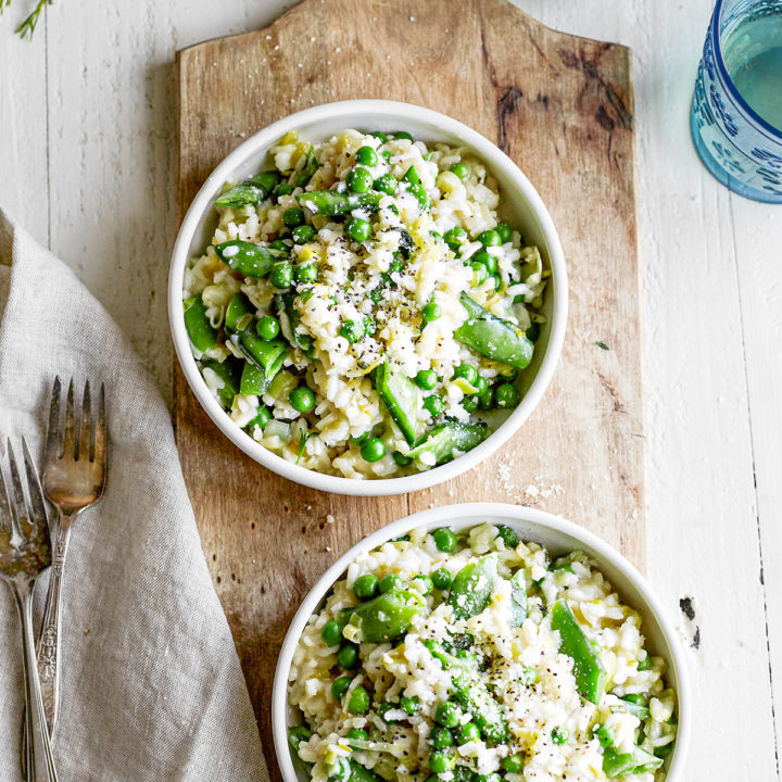 pea risotto served in two white bowls on a wooden board