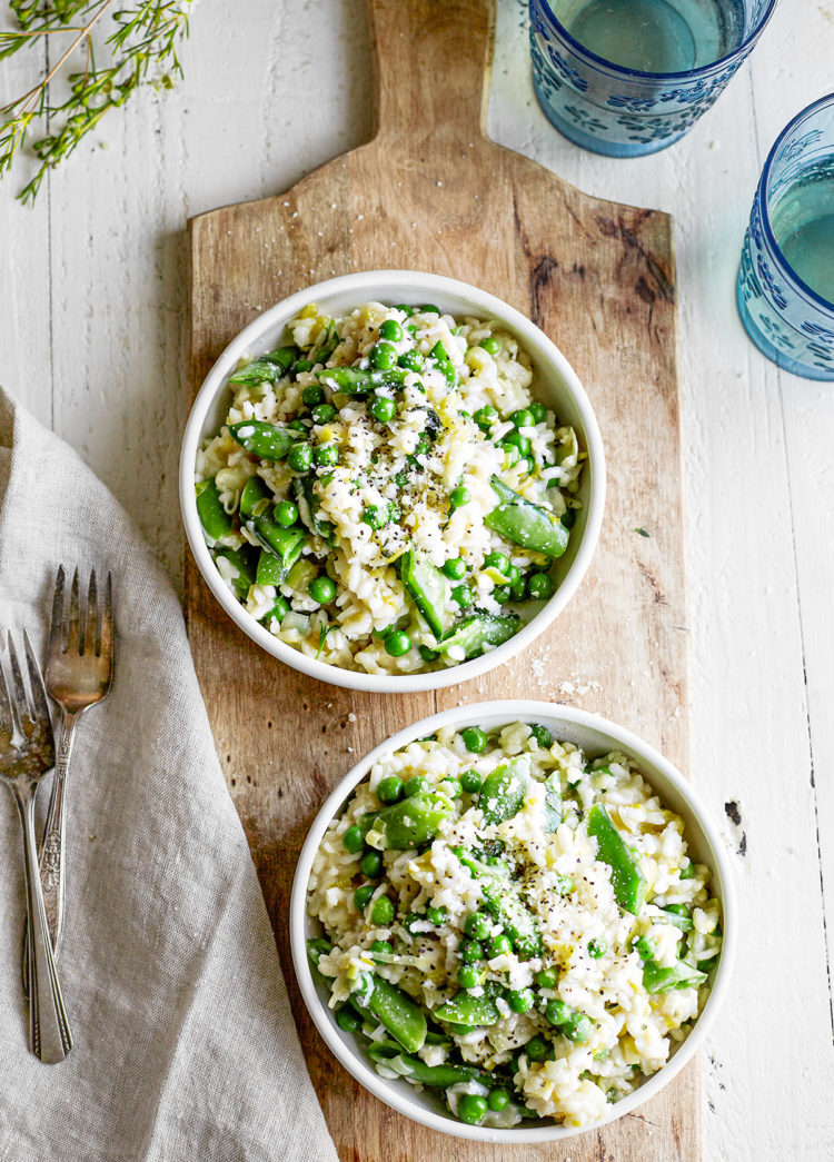 pea risotto served in two white bowls on a wooden board