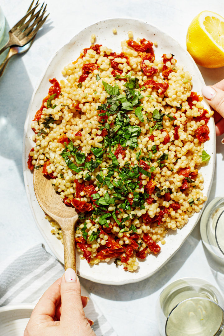 woman serving a platter of summer couscous salad
