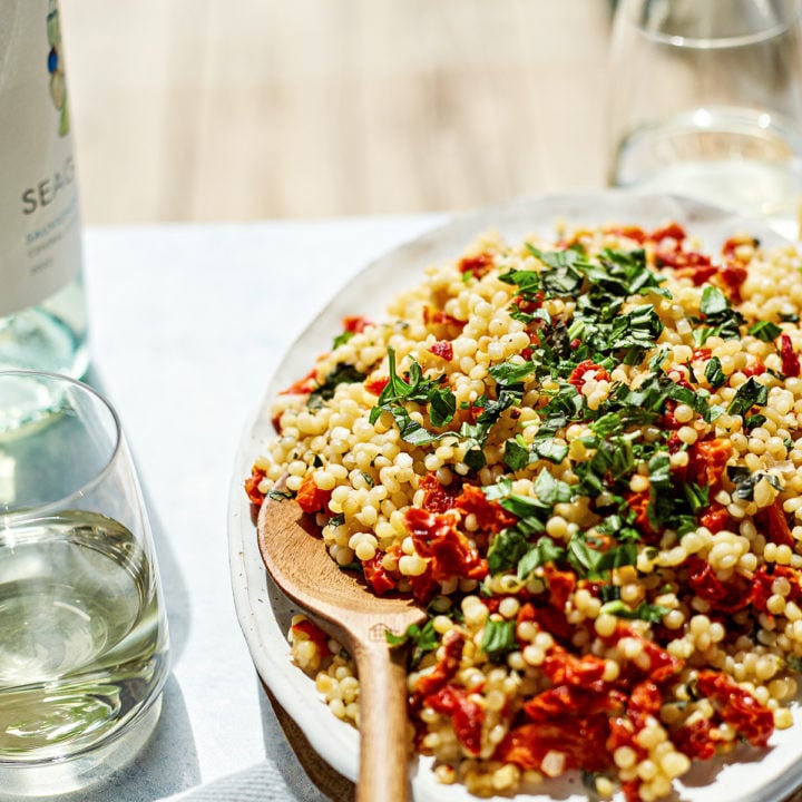 summer couscous salad on a platter with wooden spoon